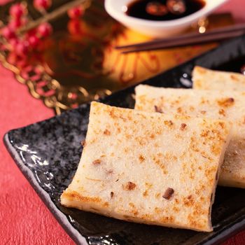 Chinese lunar new year food concept, Delicious turnip radish cake, local cuisine in restaurant with soy sauce on red background, close up, copy space