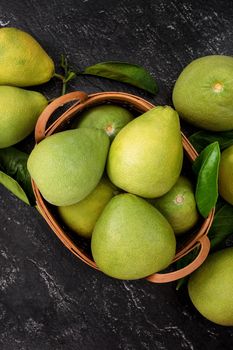 Fresh peeled pomelo, pummelo, grapefruit, shaddock on dark background in bamboo basket. Autumn seasonal fruit, top view, flat lay, tabletop shot.