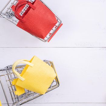 Abstract design element, annual sale, shopping season concept, mini cart with colorful paper bag on white wooden table background, top view, flat lay