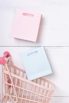 Abstract design element, annual sale, shopping season concept, mini cart with colorful paper bag on white wooden table background, top view, flat lay