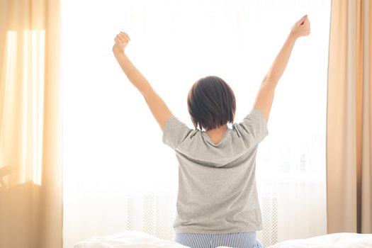 Woman stretching in bed after wake up, back view