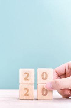 Abstract 2020 & 2019 New year countdown design concept - woman holding wood blocks cubes on wooden table and green background, close up, copy space.