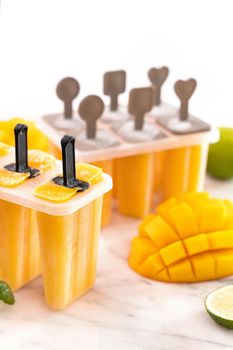 Fresh mango fruit popsicle ice in the plastic shaping box on bright marble table. Summer mood concept product design, close up.