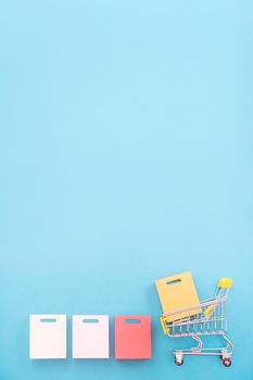 Abstract design element, concept of annual sale, shopping season - mini yellow cart with paper bag isolated on pastel blue background, top view, flat lay.