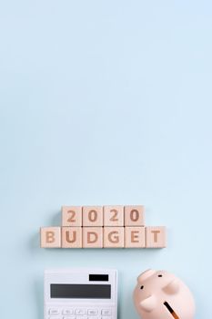 2020 goal, finance plan abstract design concept, wood blocks on blue table background with piggy bank and calculator, top view, flat lay, copy space.