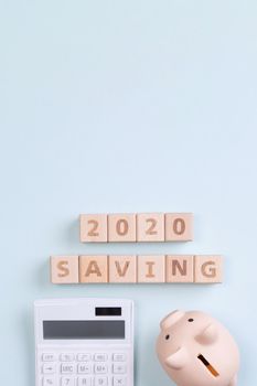 2020 goal, finance plan abstract design concept, wood blocks on blue table background with piggy bank and calculator, top view, flat lay, copy space.