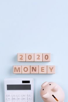 2020 goal, finance plan abstract design concept, wood blocks on blue table background with piggy bank and calculator, top view, flat lay, copy space.