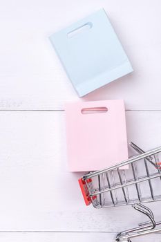 Abstract design element, annual sale, shopping season concept, mini cart with colorful paper bag on white wooden table background, top view, flat lay