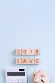 2020 goal, finance plan abstract design concept, wood blocks on blue table background with piggy bank and calculator, top view, flat lay, copy space.