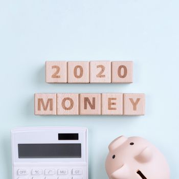 2020 goal, finance plan abstract design concept, wood blocks on green table background with piggy bank and calculator, top view, flat lay, copy space.