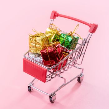 Annual sale, Christmas shopping season concept - mini red shop cart trolley full of gift box isolated on pale pink background, copy space, close up