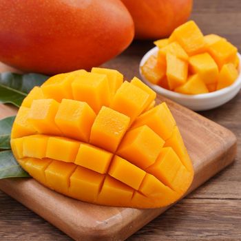 Fresh mango, beautiful chopped fruit with green leaves on dark wooden table background. Tropical fruit design concept. Flat lay. Top view. Copy space