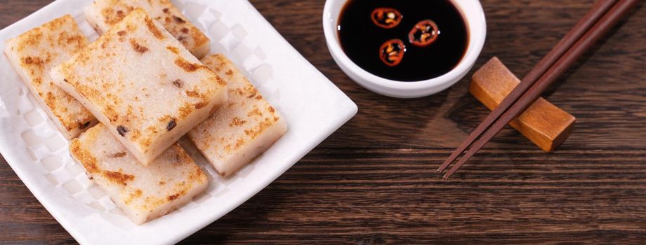 Delicious turnip cake, Chinese traditional local dish radish cake in restaurant with soy sauce and chopsticks, close up, copy space.
