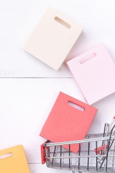 Abstract design element,annual sale,shopping season concept,mini cart with colorful paper bag on white wooden table background,top view,flat lay