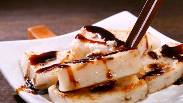 Pouring black soy sauce on ready-to-eat delicious turnip cake, Chinese traditional local dish radish cake in restaurant, close up, copy space.