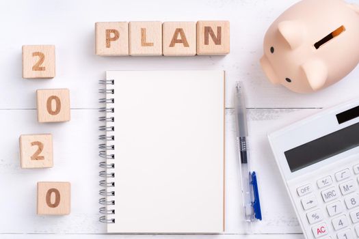 2020 goal, finance plan abstract design concept, wood blocks on white table background with piggy bank and calculator, top view, flat lay, copy space.