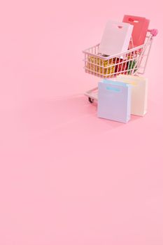 Annual sale shopping season concept - mini pink shop cart trolley full of paper bag gift isolated on pale pink background, blank copy space, close up