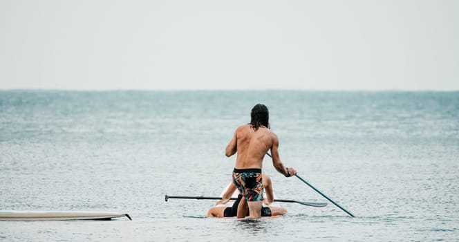 Sea woman and man on sup. Silhouette of happy young woman and man, surfing on SUP board, confident paddling through water surface. Idyllic sunset. Active lifestyle at sea or river