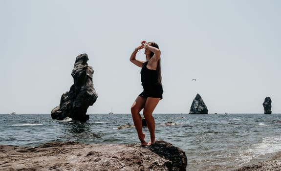 Woman travel sea. Young Happy woman in a long red dress posing on a beach near the sea on background of volcanic rocks, like in Iceland, sharing travel adventure journey