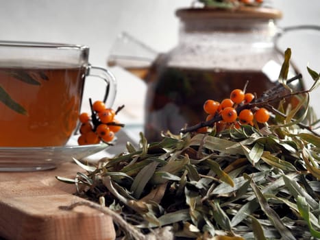Autumn. The concept of medicinal herbal tea. A pile of dry sea buckthorn leaves prepared for medicinal tea against the background of a teapot and a cup of tea. Preparations of medicinal herbs for the future.