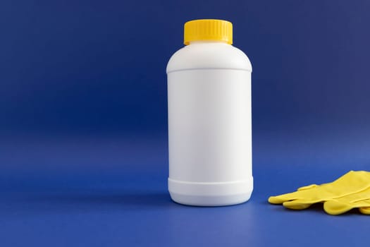 Pipe Plumber Drain Granules in White Plastic Bottle With Yellow Cap, Rubber Glove On Blue Purple Background. Clog Cleaner, Enzymes, Prevention of Blockages In Traps. Horizontal plane, Copy Space.