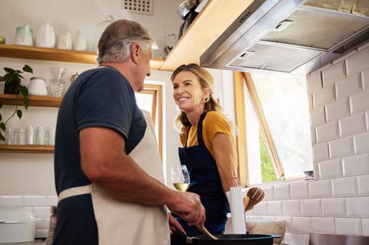 Cooking, wine and senior couple talking in the kitchen of a house while preparing dinner together. Happy, smile and elderly man and woman in communication with food and glass of alcohol in a home.