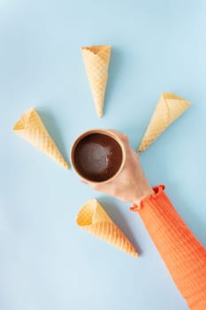 The girl holds in her hands chocolate ice cream in a craft bucket and waffle cups on the background. Blue background, copy space