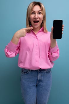 young surprised blond caucasian secretary woman with flowing hair dressed in a pink blouse and jeans holding a smartphone mockup.