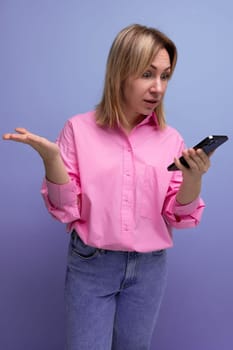 young blond woman with shoulder-length hair dressed in a fashionable pink shirt reads messages from the phone.