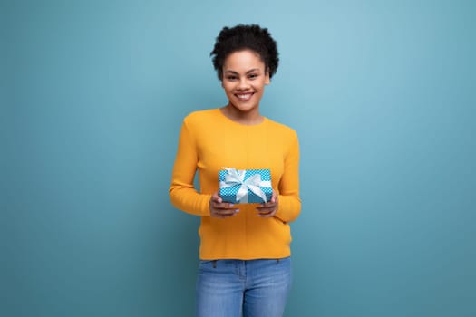 pretty joyful 20s latin woman with afro hair in casual yellow sweater got a birthday gift.