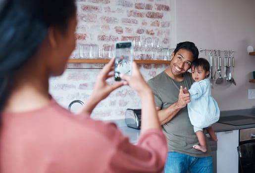 Family, care and mother with phone for photo of father and baby with down syndrome in the living room of their house. Mom taking a picture of a happy dad and child with special needs on a smartphone.