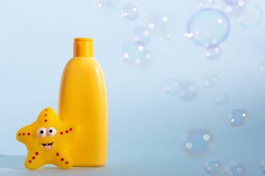 Yellow plastic bottle with baby cosmetic and funny bath toy. Soap bubbles on a background. The concept of children's hygiene