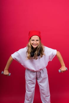 Kid girl doing fitness exercises with dumbbells on a red background