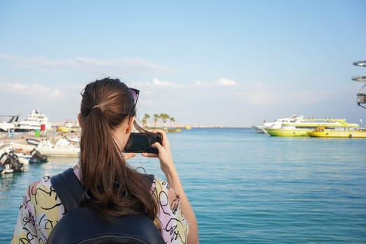 Tourist girl taking a picture of yachts at a docking bay in the sunset. High quality photo