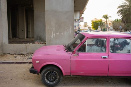 Old used pink car in front of a poor building. High quality photo