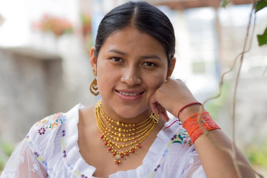 portrait of indigenous model with dress from her culture smiling at camera with her hand resting on her face. necklace, earring and bracelets. High quality photo