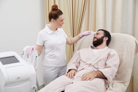 Beautician talking with young man in cosmetology cabinet