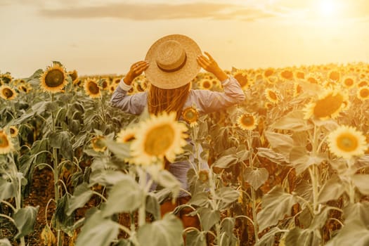 Woman sunflower field. Happy girl in blue dress and straw hat posing in a vast field of sunflowers at sunset. Summer time