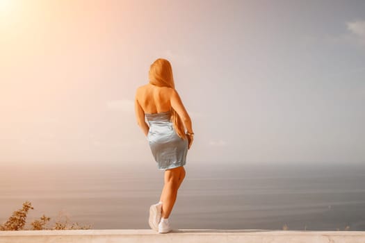 Woman travel sea. Young Happy woman in a long red dress posing on a beach near the sea on background of volcanic rocks, like in Iceland, sharing travel adventure journey