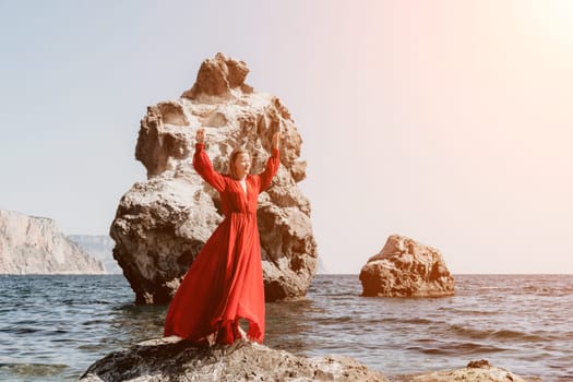 Woman travel sea. Young Happy woman in a long red dress posing on a beach near the sea on background of volcanic rocks, like in Iceland, sharing travel adventure journey