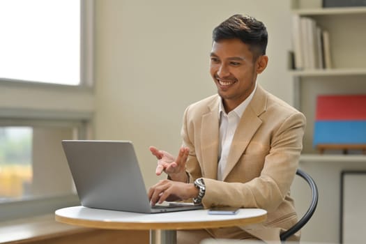 Attractive businessman in elegant suit having video call with business partner via laptop computer.