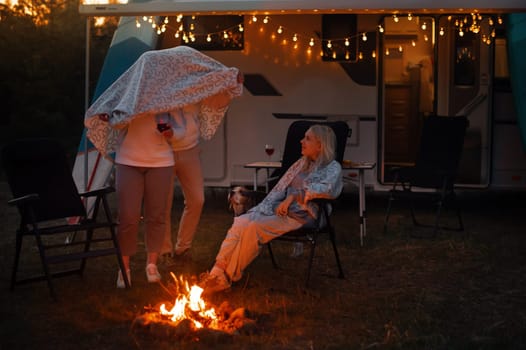 The family rests together in the evening near the campfire and their motorhome.