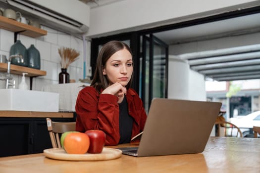 Focused young woman sitting at her kitchen table at home working on her small business with a laptop.