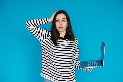 Emotional Young Woman in Striped Sweater Distraught by Bad News on Laptop - Expressive Female Feeling Sad and Disheartened - Isolated Blue Background - Perfect for Conceptual, Emotional,