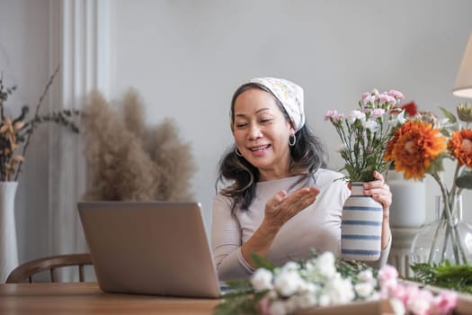 Happy and attractive mature Asian woman enjoying with her online flower arrangement workshop at home...