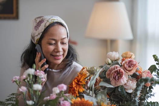 Happy and attractive mature Asian woman enjoying with her online flower arrangement workshop at home...
