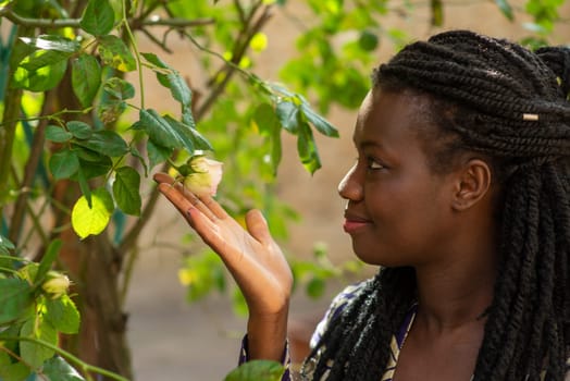 Portrait Young beautiful relaxed african woman wearing summer outfit in the garden enjoy flowers, dreadlock hairtstyle.