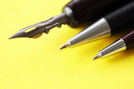 Three various pens closeup on yellow paper background