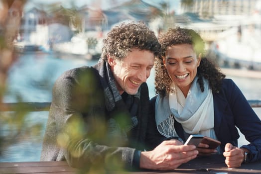 Couple, phone and talking outdoor for travel, communication and 5g network connection on a bridge. Happy interracial man and woman together on vacation with a smartphone for location internet search.