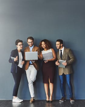 Studio shot of a group of businesspeople using wireless technology together while standing in line against a gray background.